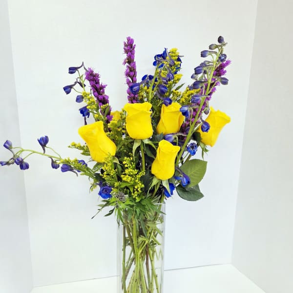 Yellow roses and blue-purple flowers in a clear glass vase