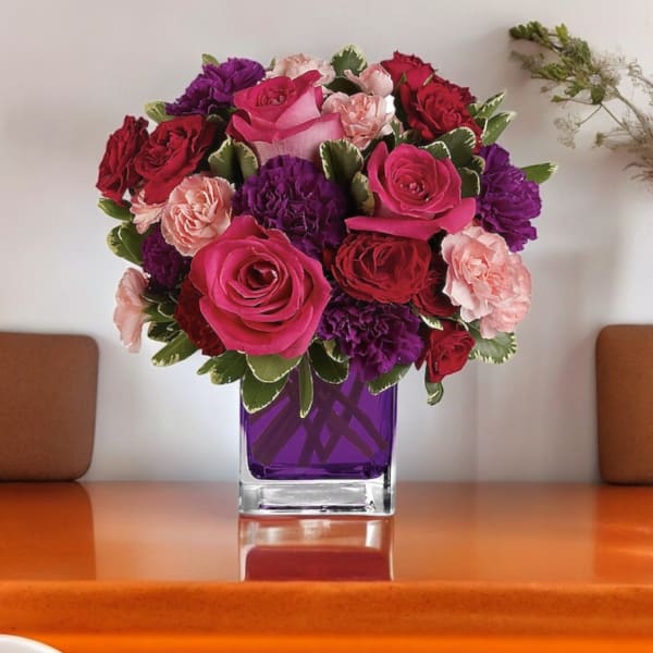 Pink, red, and purple flowers arranged in a square glass vase