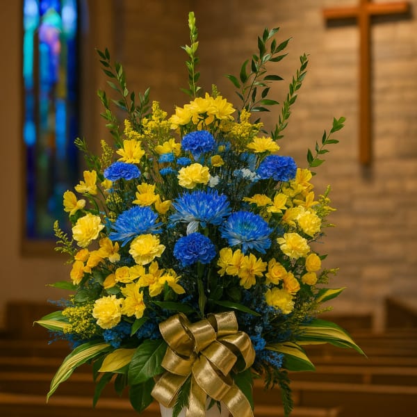 Blue and yellow floral arrangement in a white vase with a gold ribbon