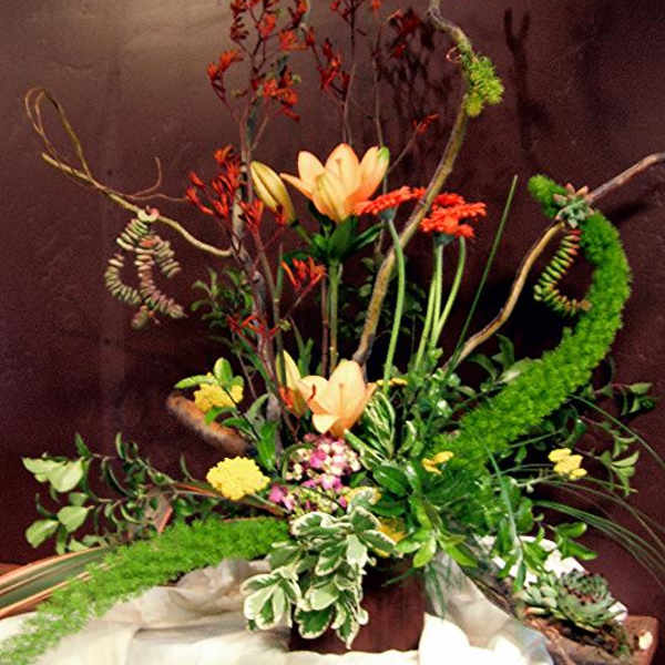 Tall floral arrangement with peach lilies and red-orange blooms