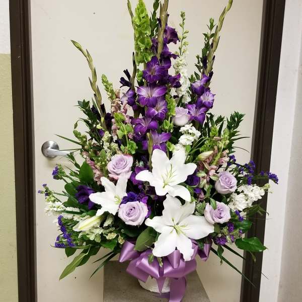 Tall floral arrangement with white lilies, purple roses, and purple spikes in a vase