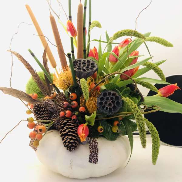 Autumn floral arrangement in a white pumpkin-shaped container with pinecones and cattails