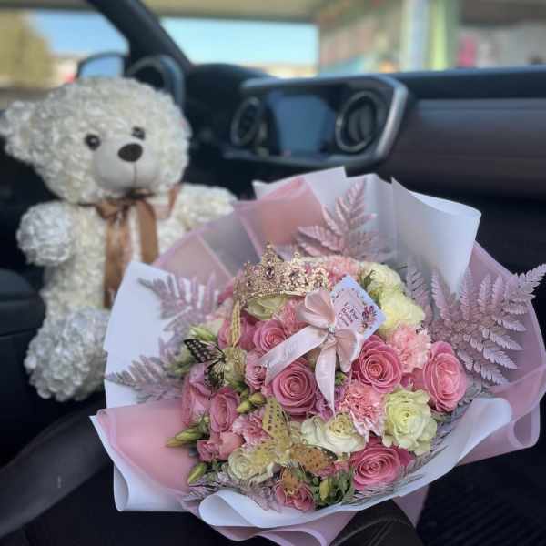 Pink and white rose bouquet with a teddy bear and crown in a car seat