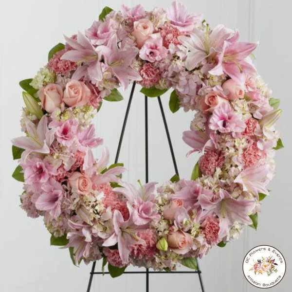 Pink and white floral wreath of lilies, roses, carnations, and hydrangeas on a black stand