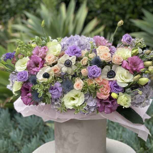 Pastel bouquet of roses, lisianthus, hydrangeas, and anemones in a hatbox