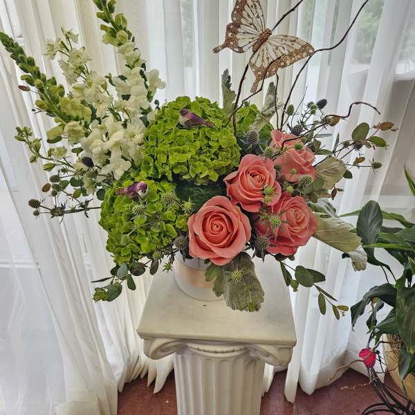 Pink roses and green hydrangeas in a white vase with a butterfly accent