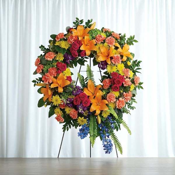 Large floral wreath on a stand with orange lilies, roses, and mixed blooms
