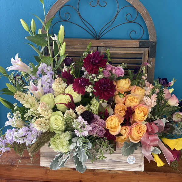 Large mixed flower arrangement in a wooden box with a pink ribbon