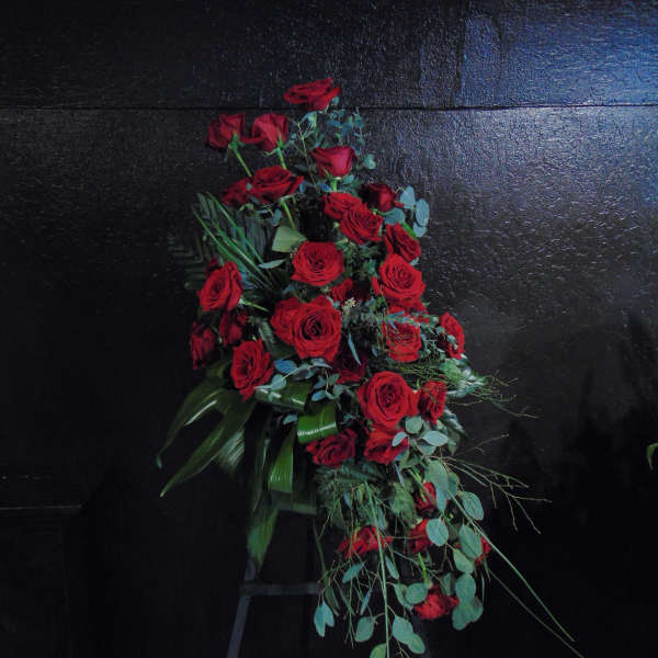 Tall standing spray of red roses arranged in a cascading shape on a black stand.