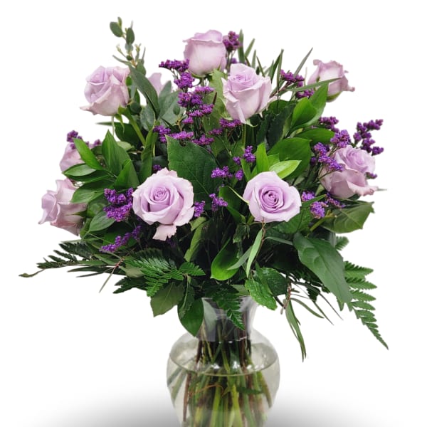 Lavender roses and small purple flowers arranged with lush foliage in a clear glass vase