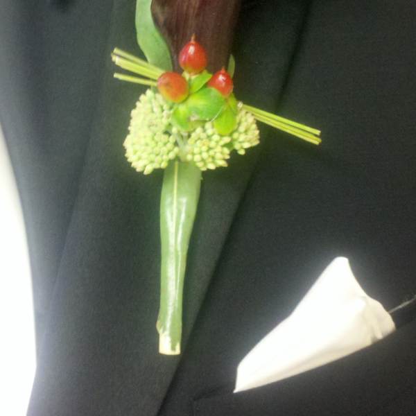 Dark calla lily boutonniere with green berries on a black suit lapel