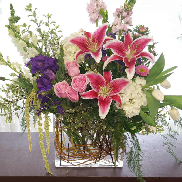 Mixed bouquet with pink lilies, roses, and purple blooms in a glass vase