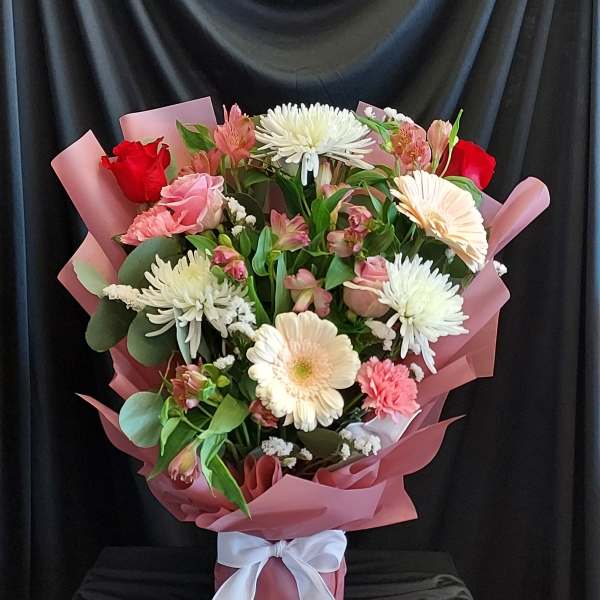 Mixed bouquet of pink and white flowers wrapped in pink paper with a white ribbon