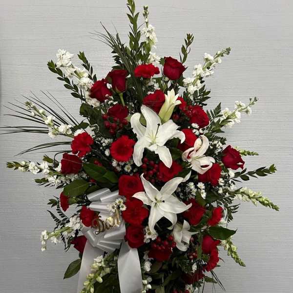Standing floral spray with red roses and white lilies on a white ribboned easel