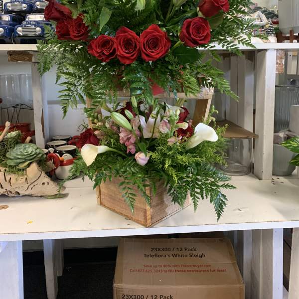 Two floral arrangements with red roses, lilies, and calla lilies in wooden boxes