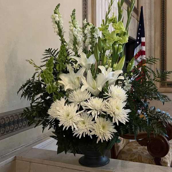 Tall white floral arrangement with lilies and chrysanthemums in a dark vase