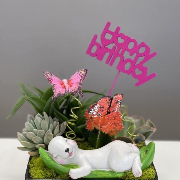 Succulent planter with a sleeping baby figurine and a pink "baby boy" topper
