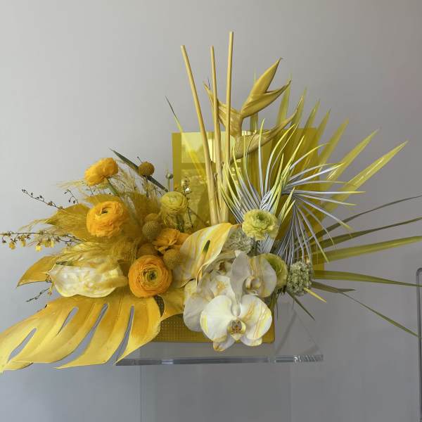 Yellow floral arrangement with orchids and tropical leaves in a rectangular container