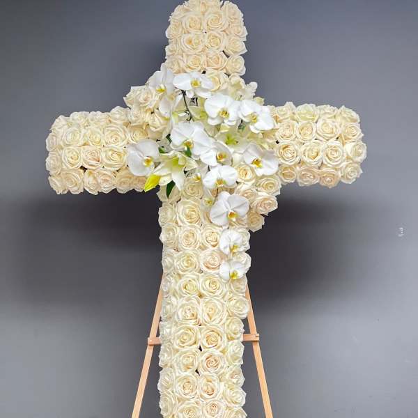 Cross-shaped floral tribute of cream roses with white orchids on an easel