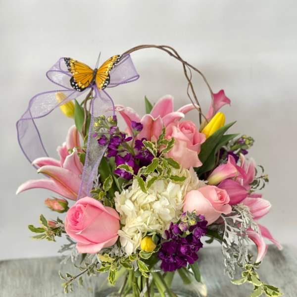 Pink and purple flower arrangement in a glass vase with a butterfly bow