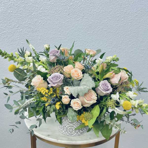 Mixed bouquet of pastel roses and yellow blooms in a decorative white vase