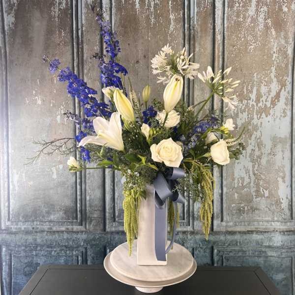 Tall floral arrangement with white lilies, roses, and blue delphinium in a vase