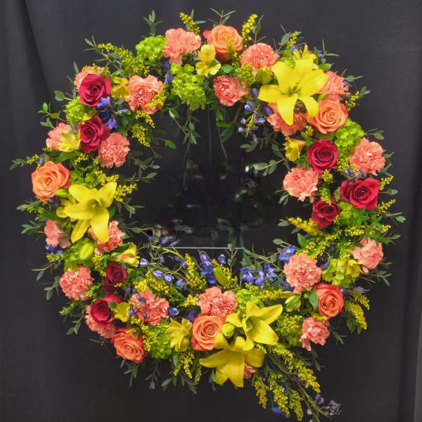 Circular floral wreath with roses, carnations, and lilies on a dark background