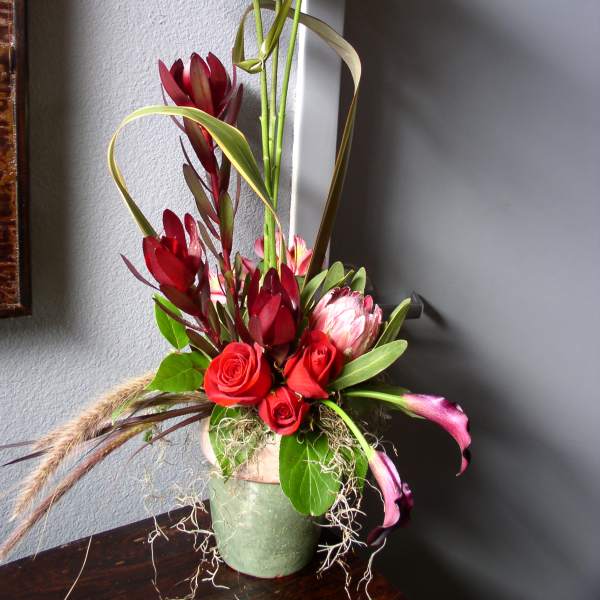 Tall floral arrangement with red roses and pink blooms in a green vase