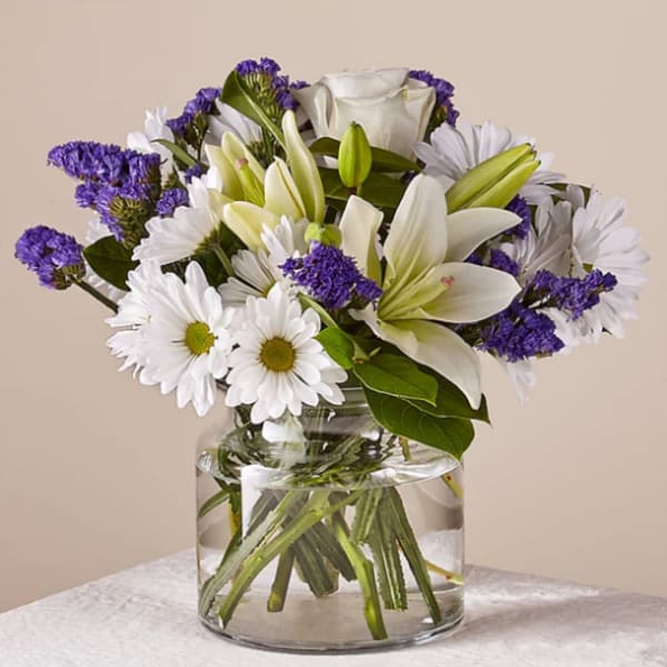White lilies and daisies with purple filler in a glass vase