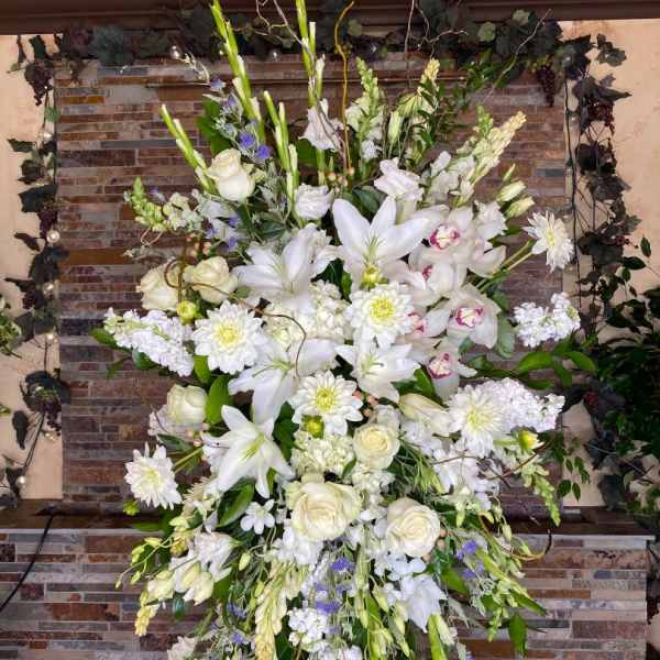 Tall white floral spray with lilies, roses, and daisies