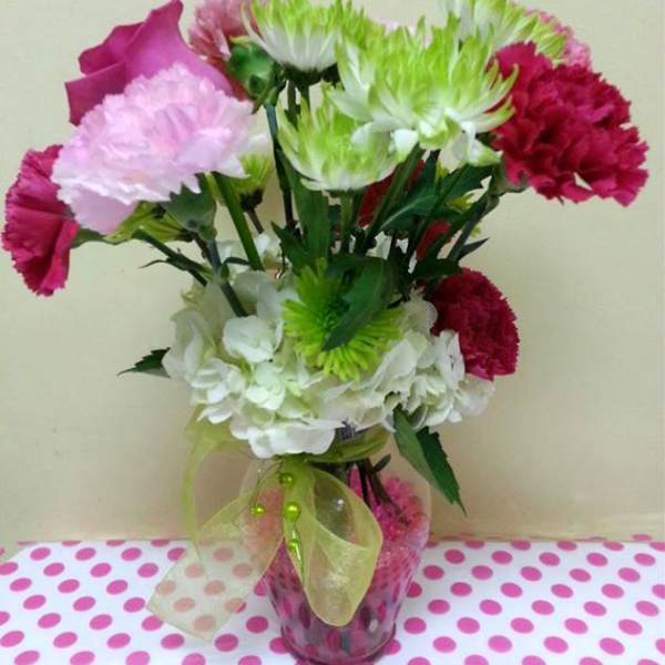 Pink, white, and green carnations in a glass vase with a ribbon