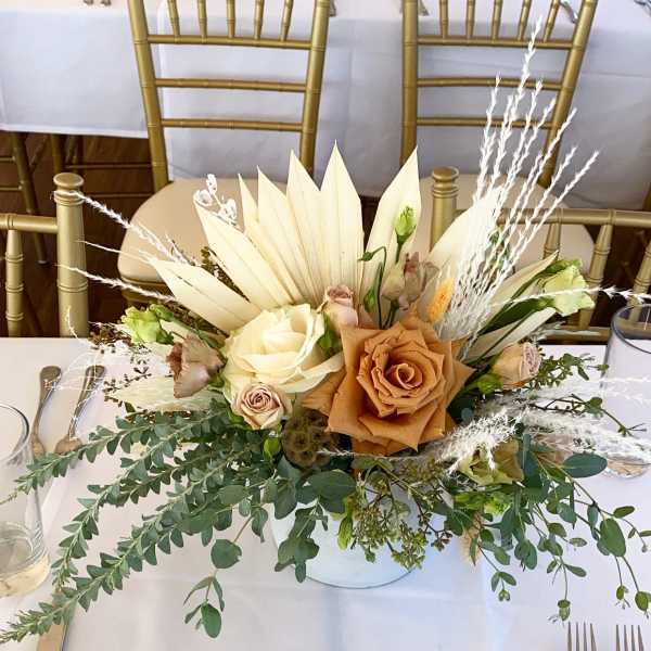 Low floral centerpiece with cream and tan roses on a white table