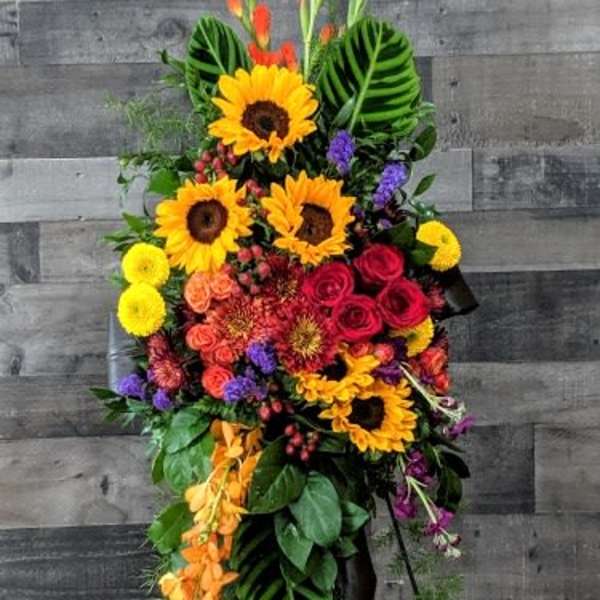 Tall standing spray of sunflowers, red roses, and bright mixed flowers on a metal easel.