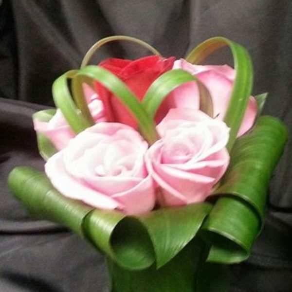 Small bouquet of pink and red roses wrapped with green ribbon loops