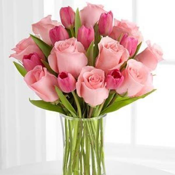 Pink roses and tulips arranged in a clear glass vase