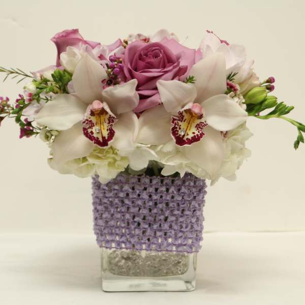 Pink roses and white orchids in a clear square vase with a purple wrap