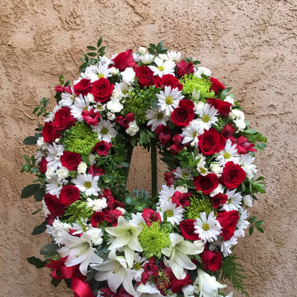 Circular wreath of red roses, white daisies, and lilies with a red ribbon