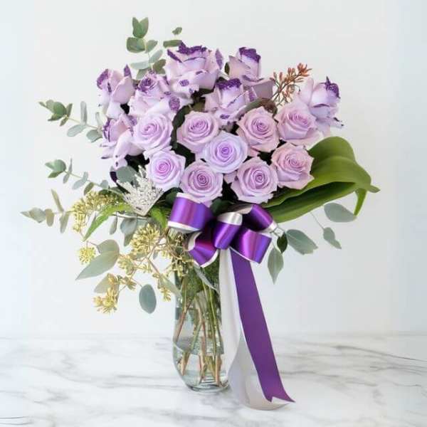 Tall arrangement of lavender roses with purple ribbon in a clear glass vase