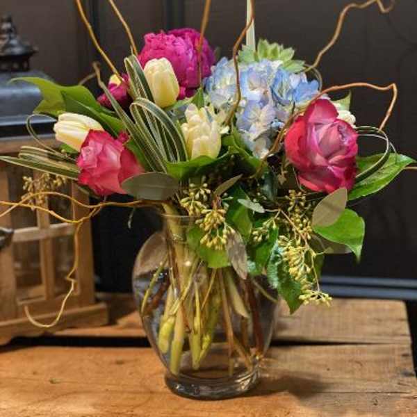 Mixed bouquet of pink, white, and blue flowers in a glass vase