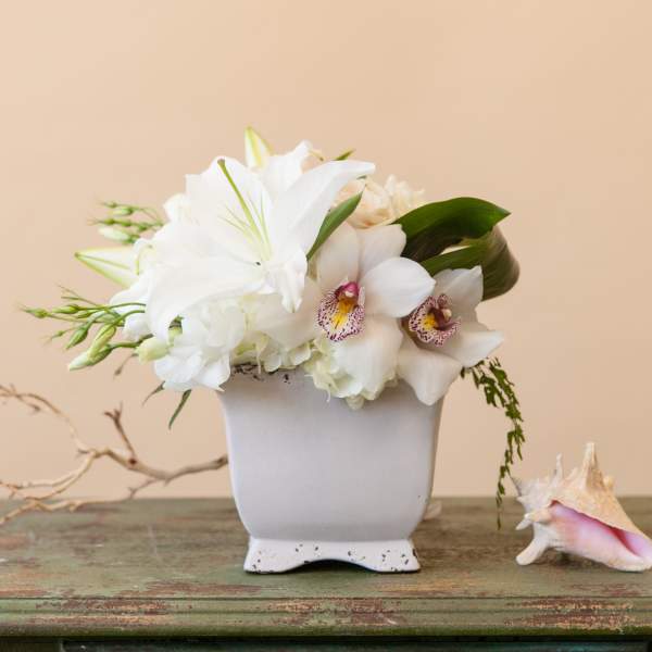 White floral arrangement in a white vase with a seashell beside it