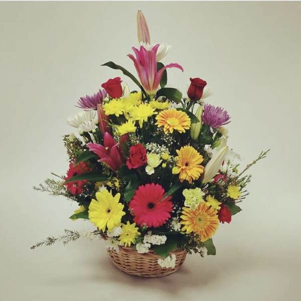 Mixed bouquet in a wicker basket with lilies, roses, and daisies