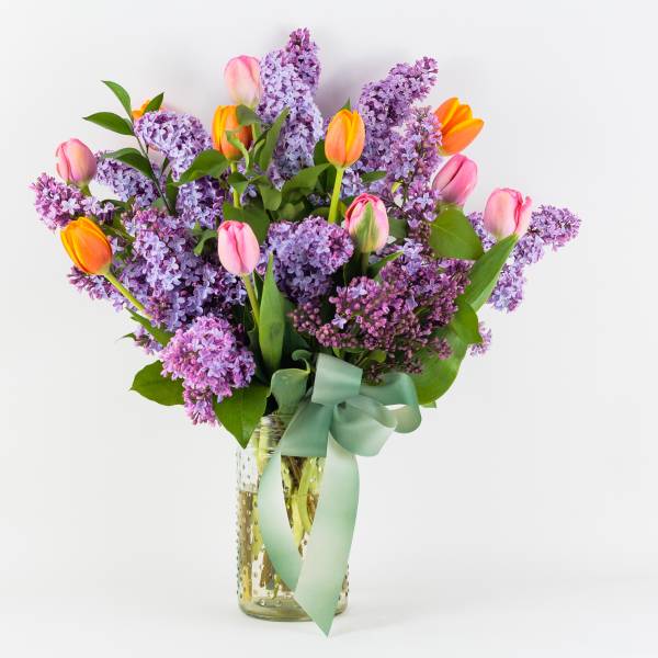 Bouquet of purple lilacs and pink tulips in a glass vase with a ribbon