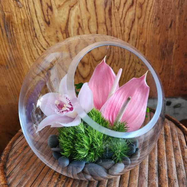 Pink orchid and calla lilies in a clear glass orb with stones