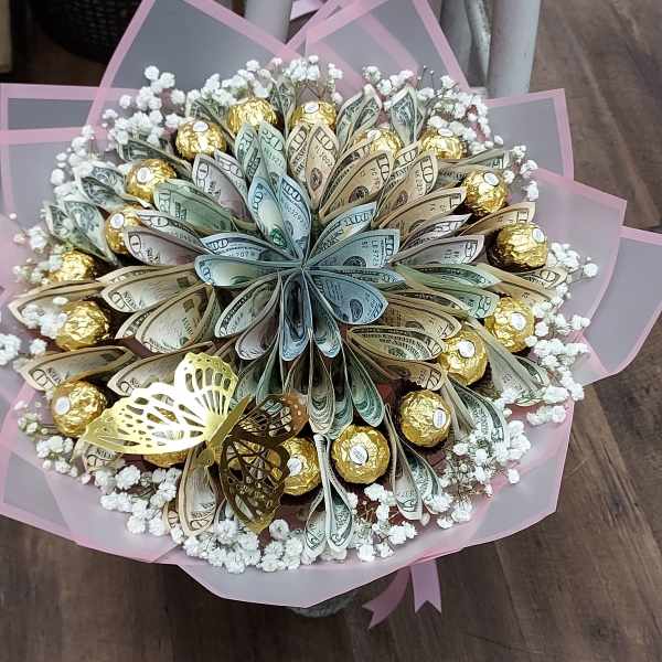 Bouquet of folded money and gold-wrapped chocolates with small white blooms, wrapped in pink paper