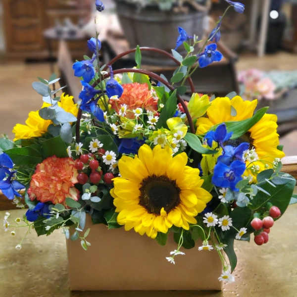 Bright sunflower arrangement in a cardboard box with blue and orange flowers