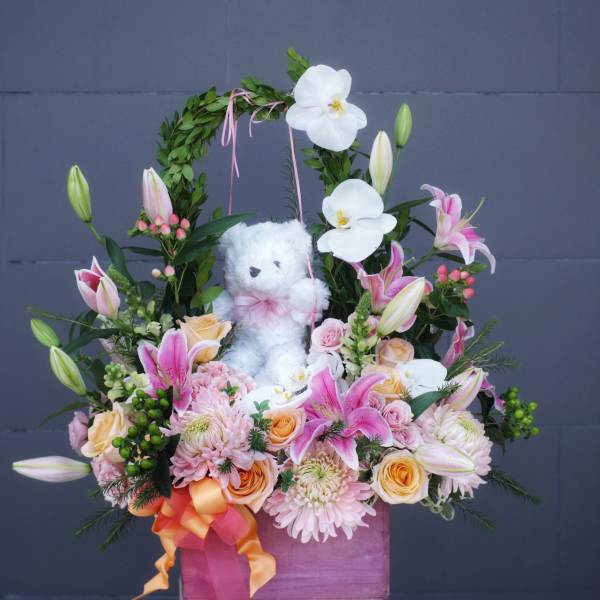 Pink and white floral arrangement with a teddy bear in a pink box