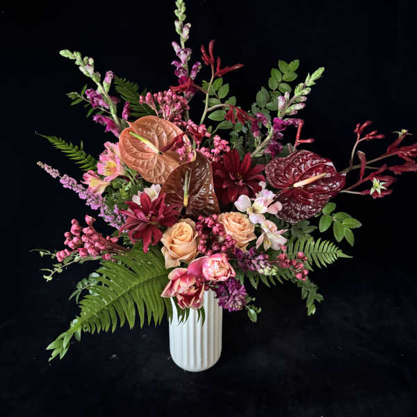 Mixed bouquet in a white vase with pink, burgundy, and peach blooms