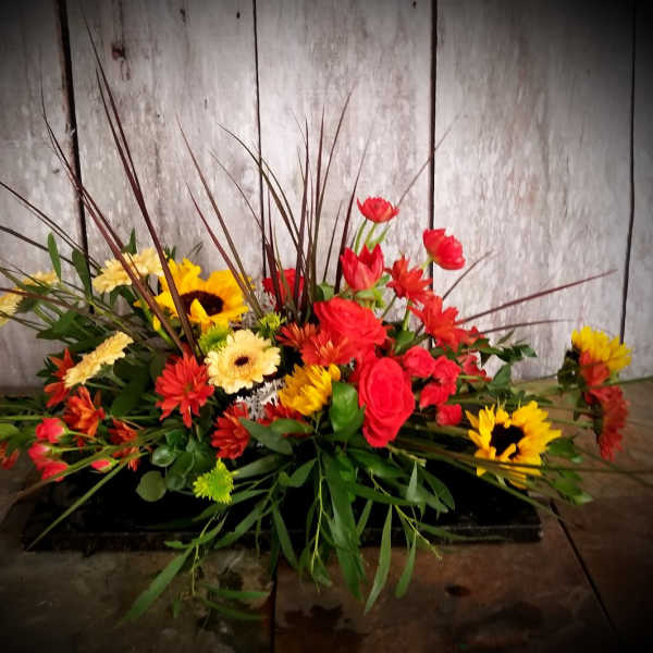 Low floral arrangement with red, yellow, and orange blooms in a black container