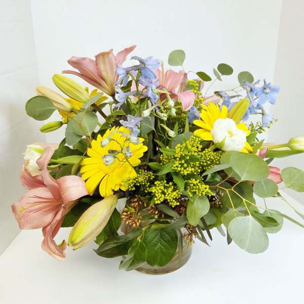Mixed bouquet of lilies, daisies, and blue flowers in a glass vase