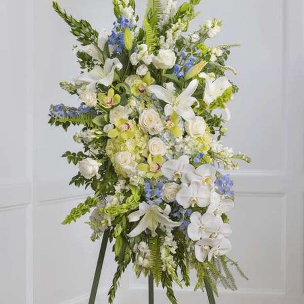 Tall white and green floral standing spray with blue accents on an easel